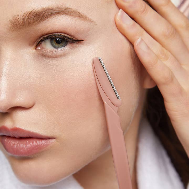 A woman using a dermaplaner on her face, gently exfoliating her skin for a radiant complexion.